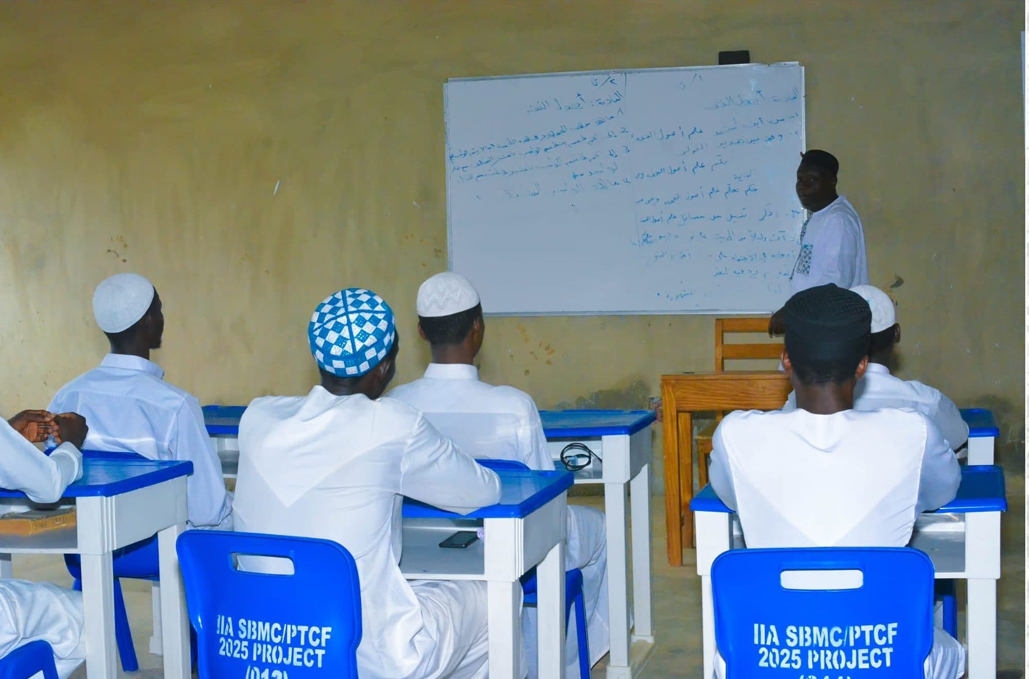 A teacher explaining Arabic text on the whiteboard to a class of boys