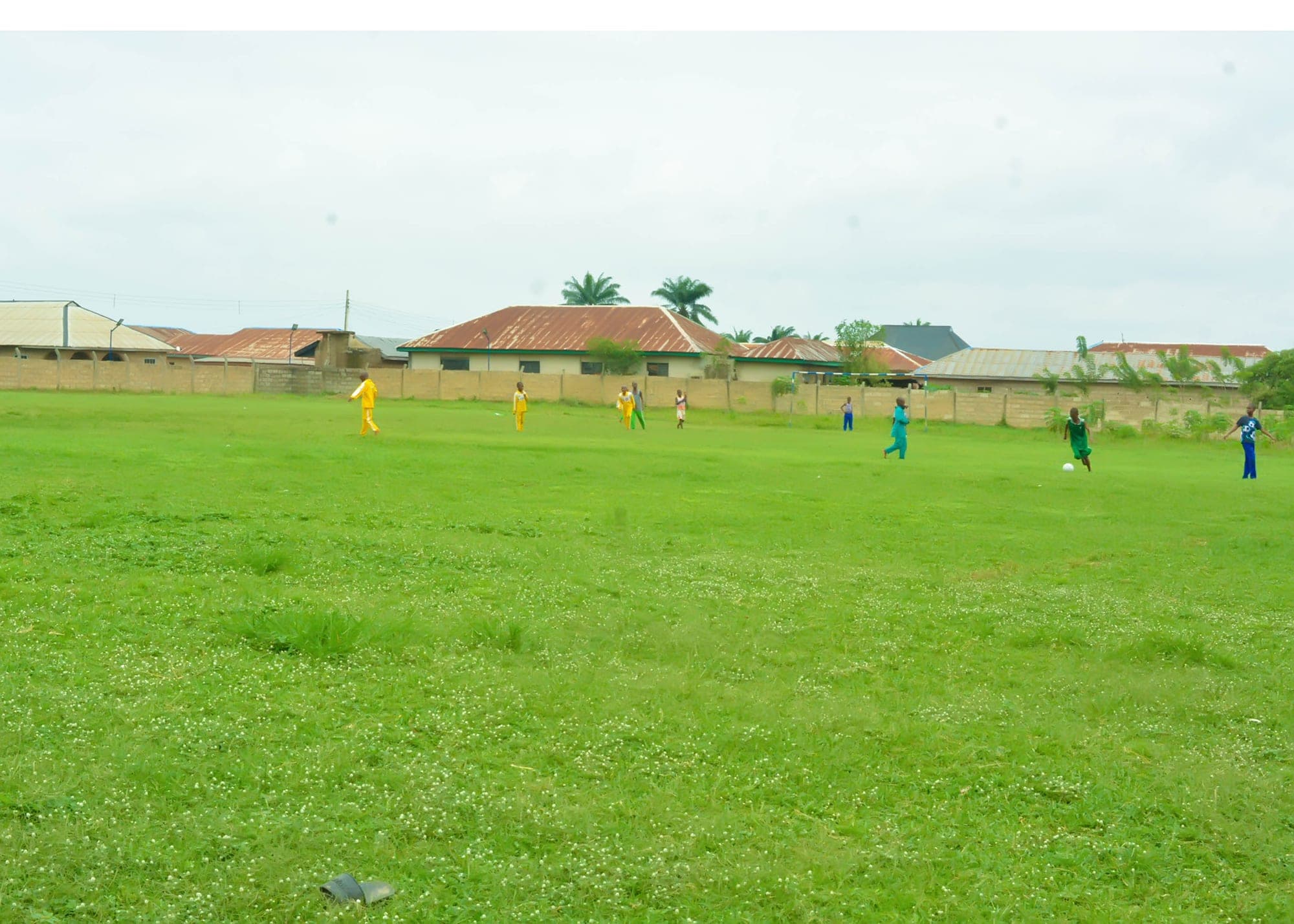 The wide green school sports field with pupils playing in the distance