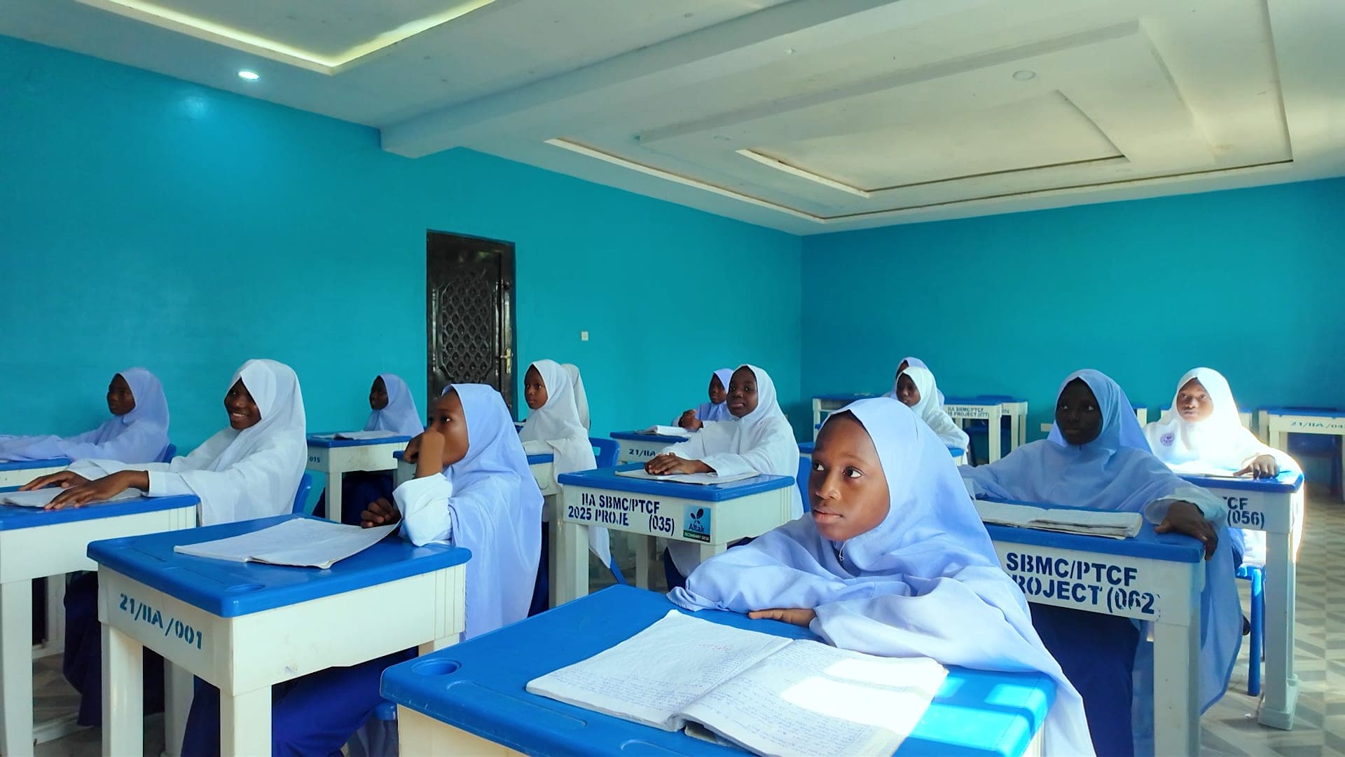 Girls in white hijabs studying at desks in a bright blue classroom