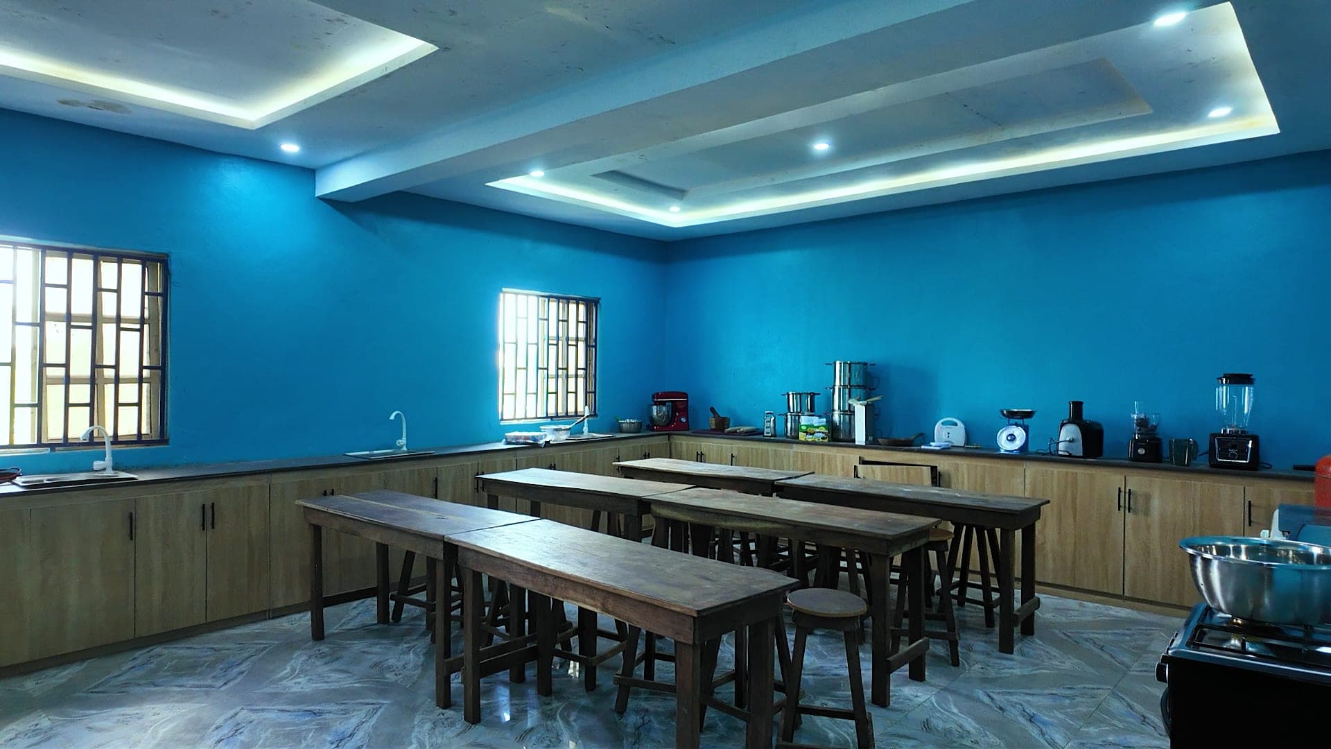 A bright practical room with long tables and fitted kitchen counters