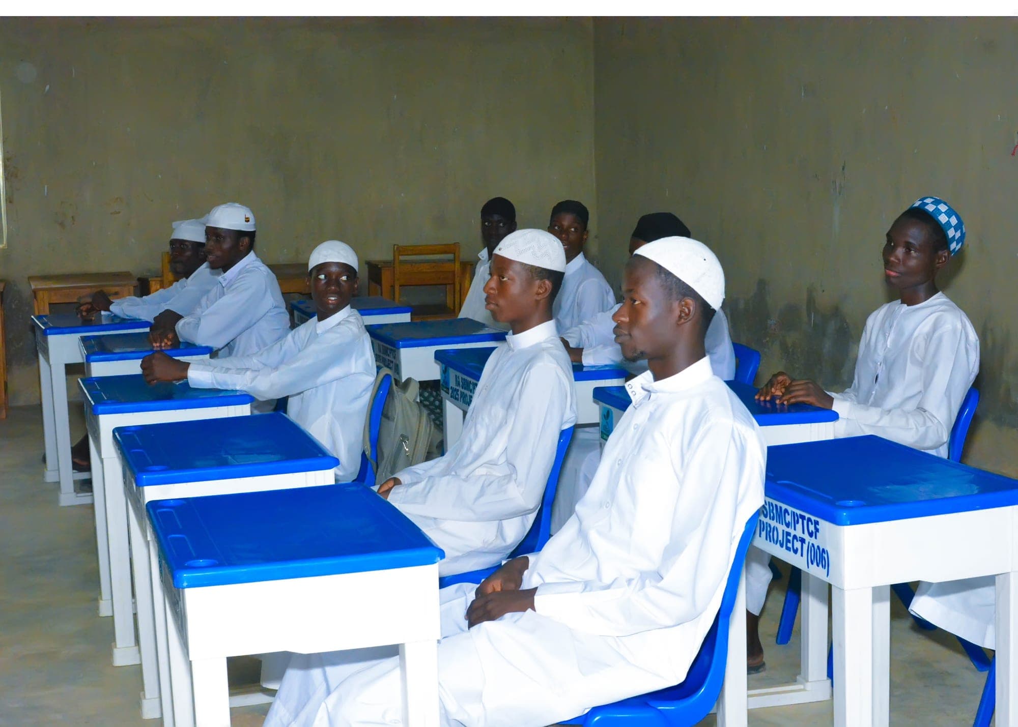 Senior Inaayatullah boys in white robes and caps seated at their desks in class