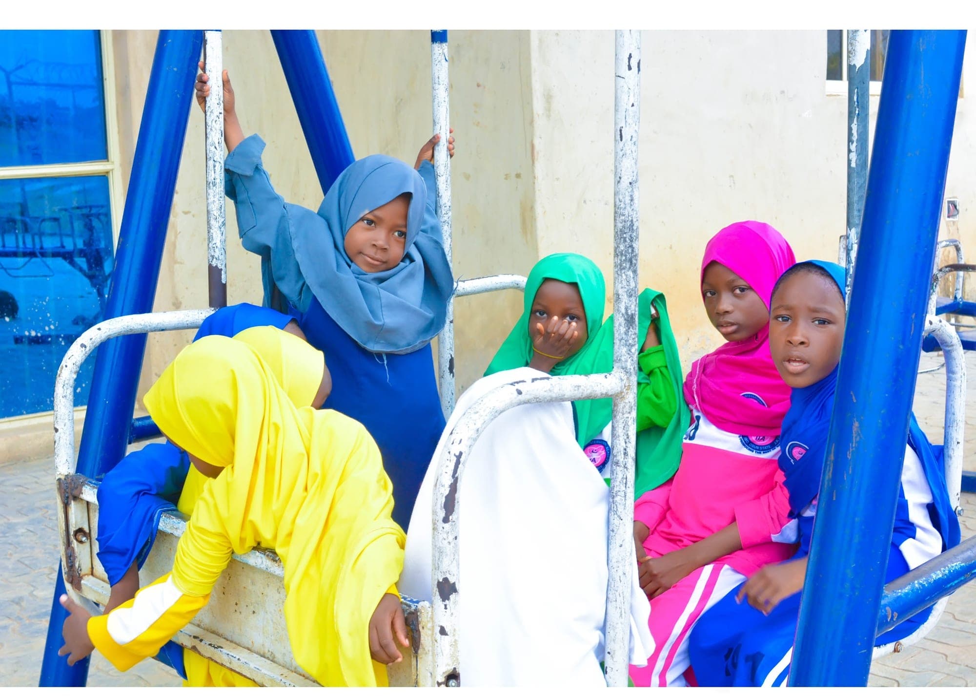 Girls in bright hijabs gathered around a playground swing