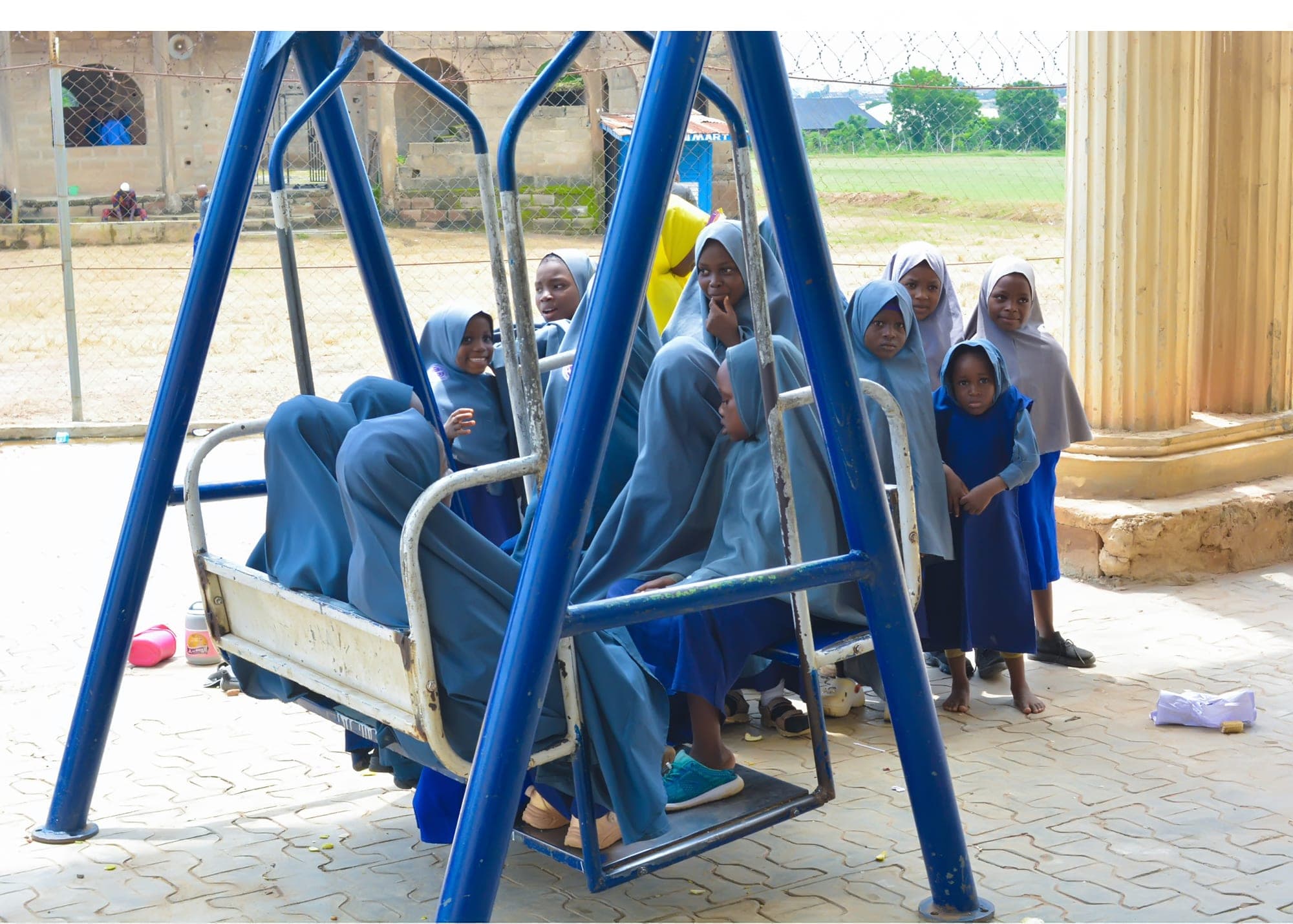 Pupils in blue hijabs sharing a playground swing