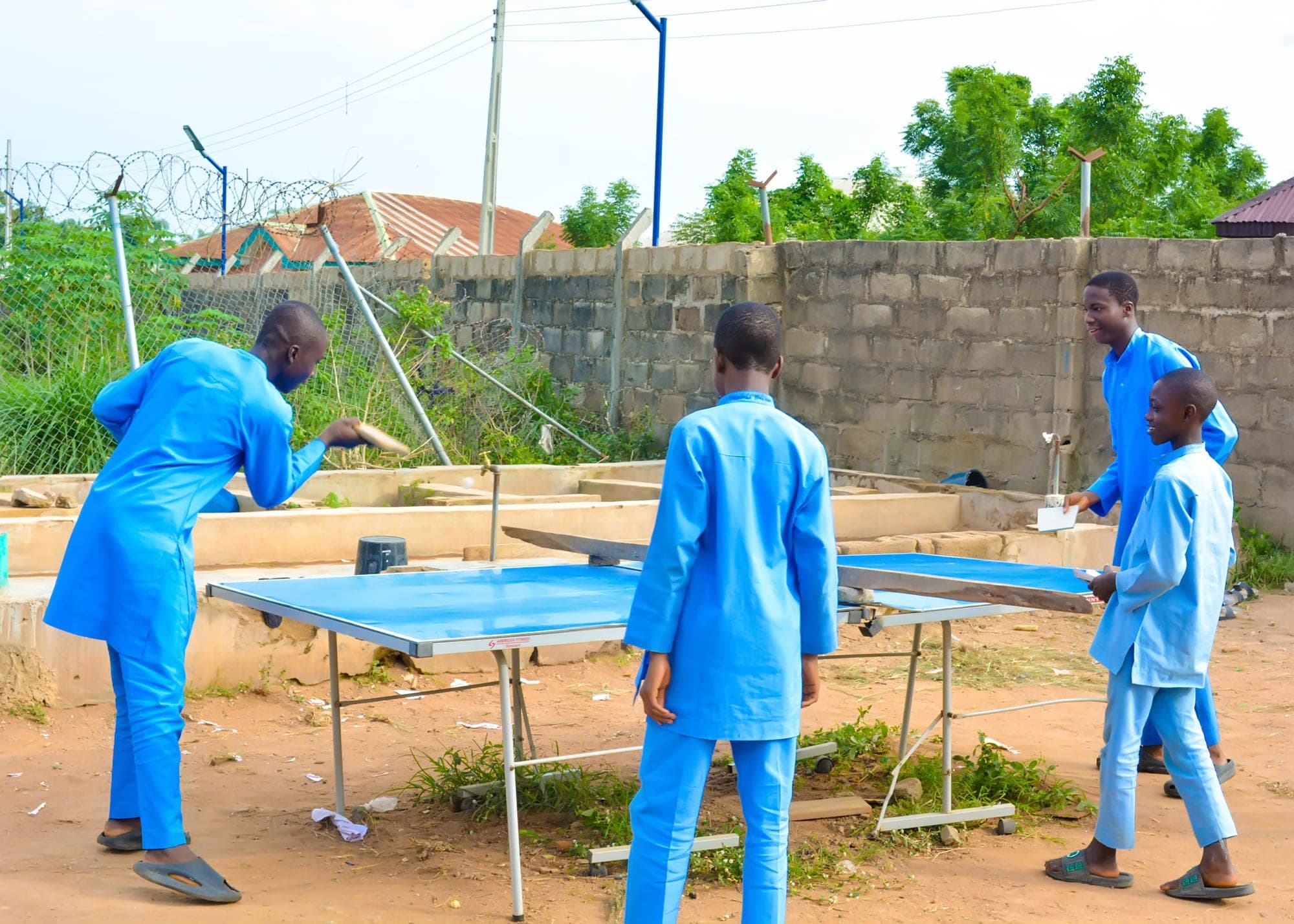 Boys in blue uniforms playing table tennis on an outdoor table