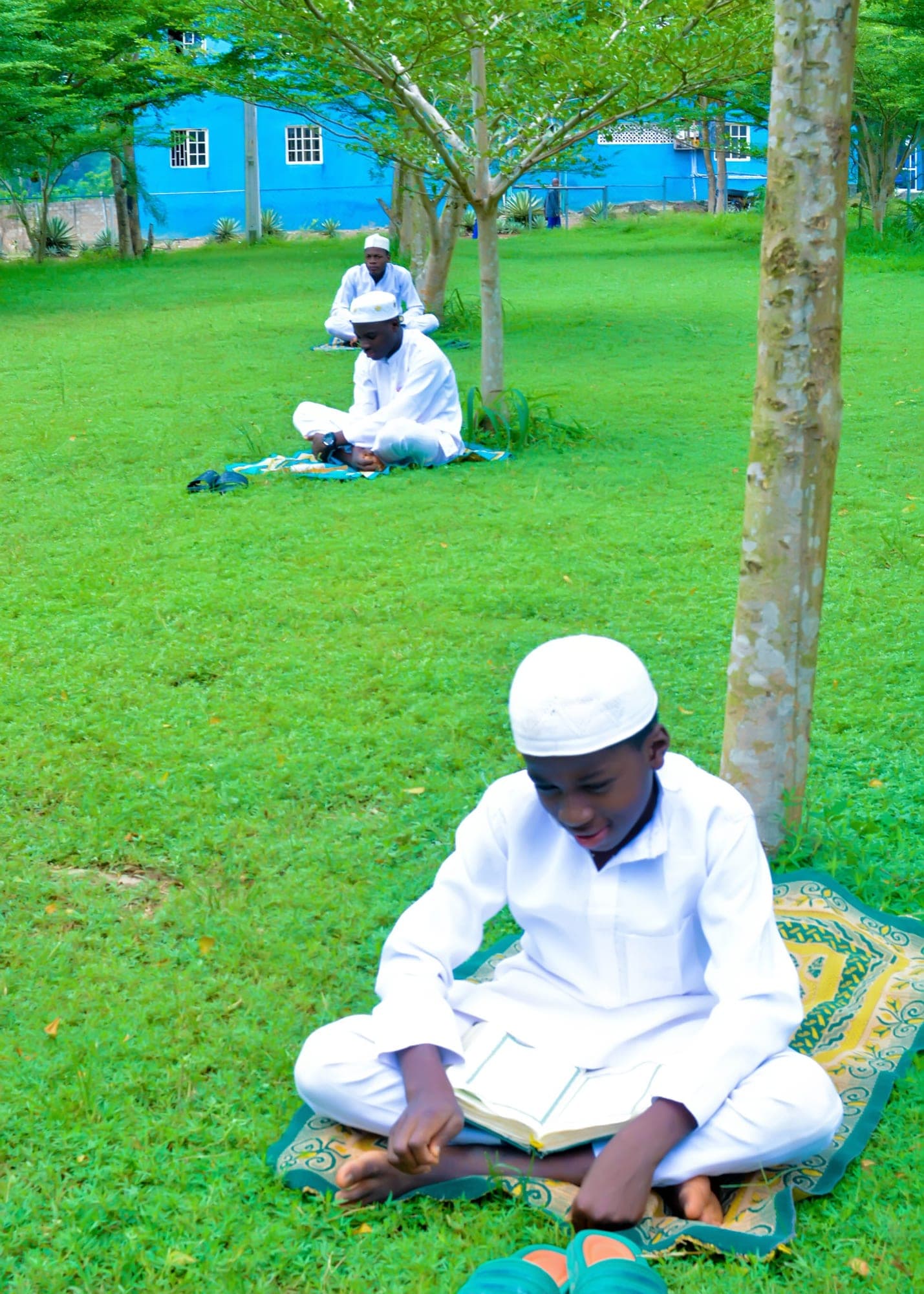 A Tahfiz student reciting the Qur’an on a mat beneath a tree