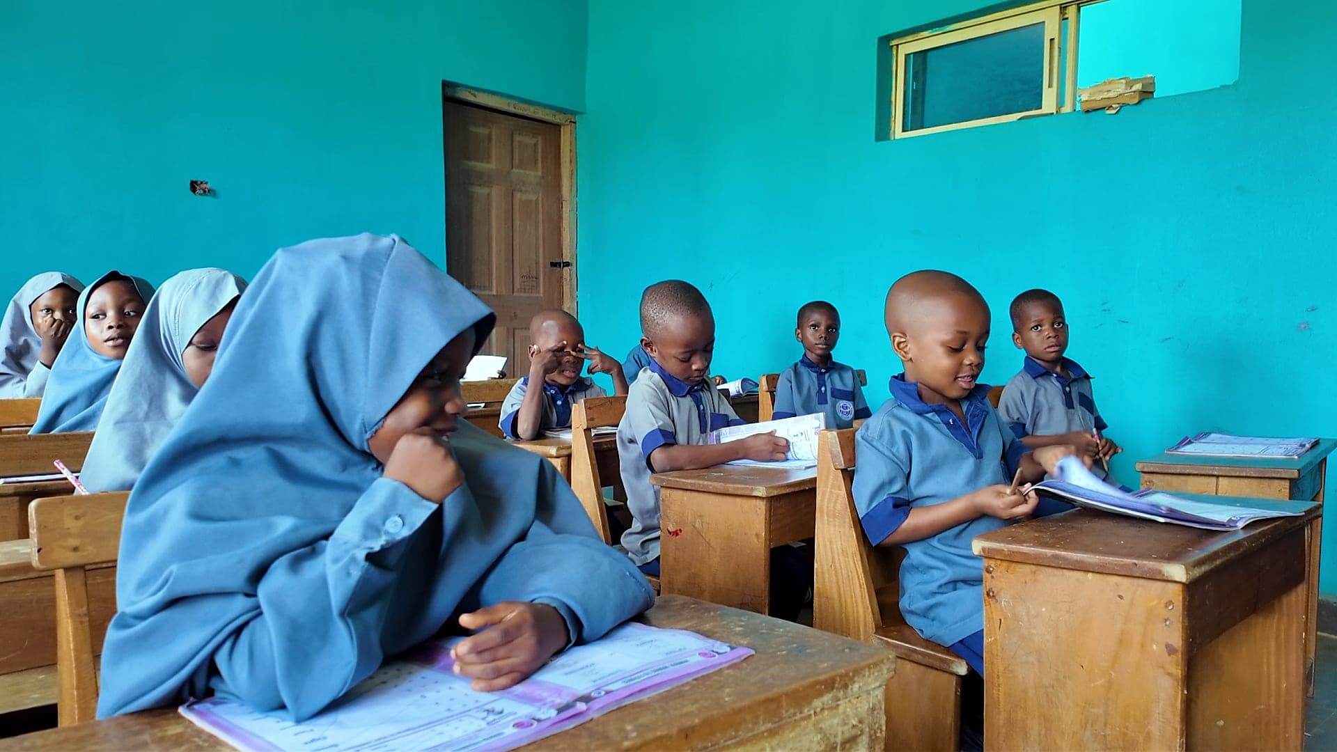 Young pupils reading and writing at wooden desks in a bright classroom